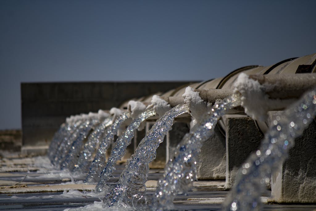 Contact Close-up view of water flowing from industrial pipes against a clear blue sky.